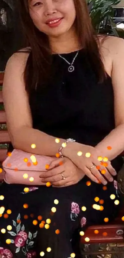 Woman in black floral dress sitting on bench with warm lighting.