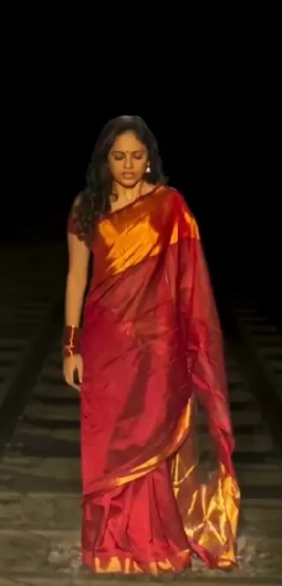 Woman in red sari walking on railway track at night.