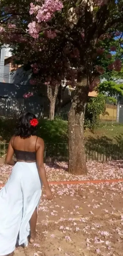 Woman walking under pink cherry blossom in garden.