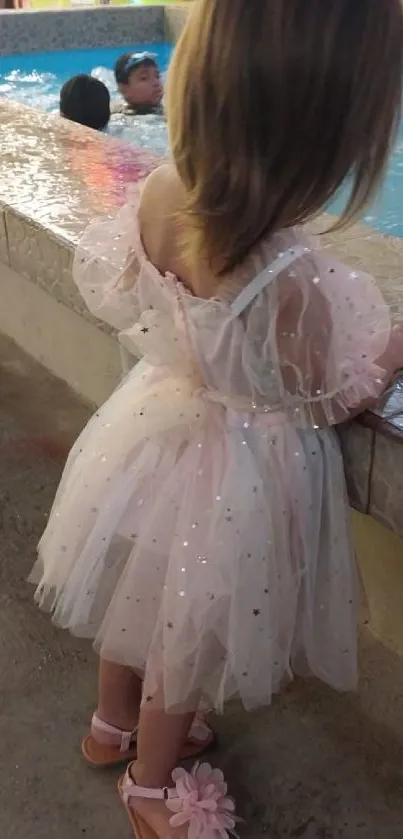 Child in sparkly pink dress by a poolside.