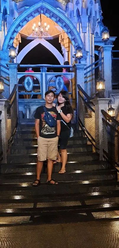 Couple standing on illuminated castle stairs at night.