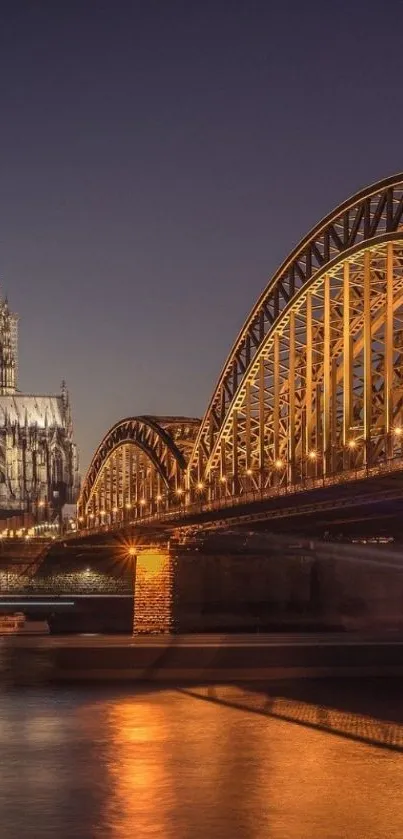 Night view of an illuminated bridge and cathedral reflecting on water.