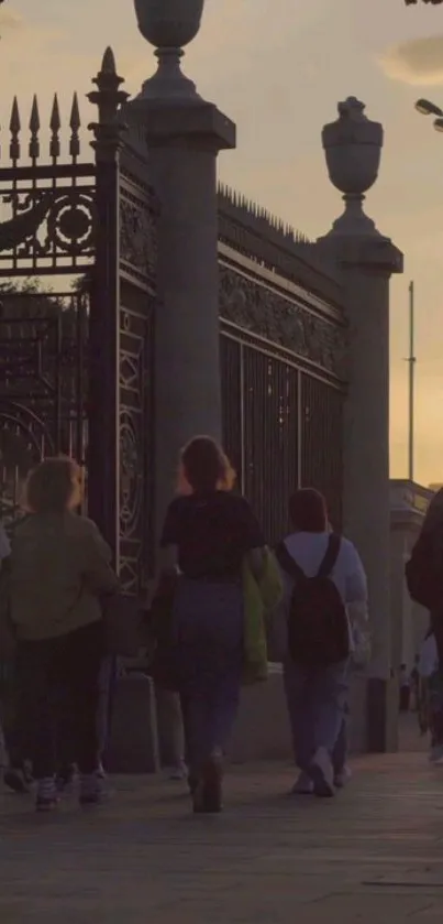 Silhouetted figures walking by fence at sunset in urban setting.