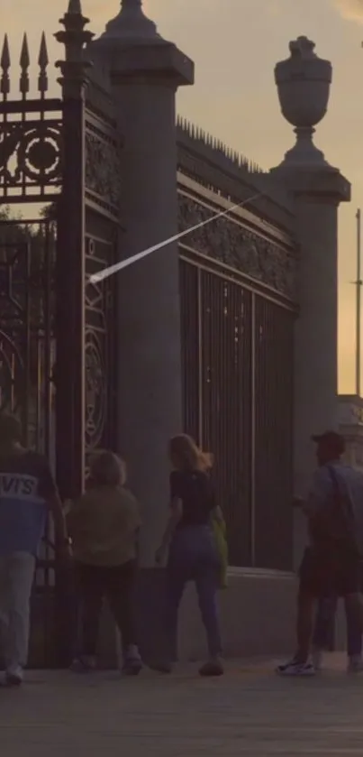 Silhouettes walking past a city fence at sunset.