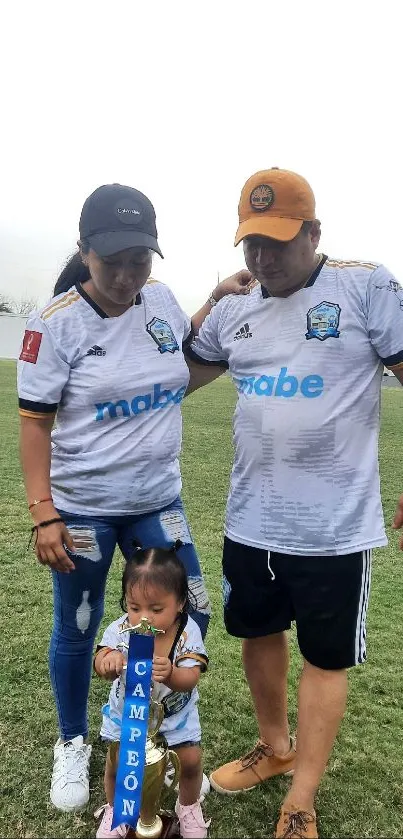 A family celebrates winning a soccer tournament with a trophy on the field.