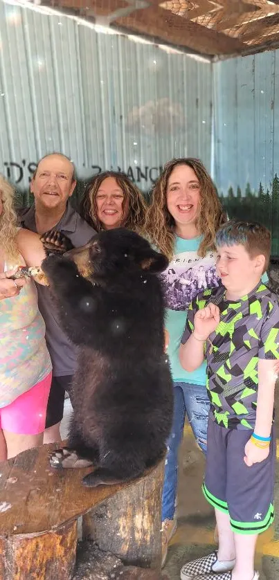 Family enjoys playful moment with bear cub in rustic outdoor setting.