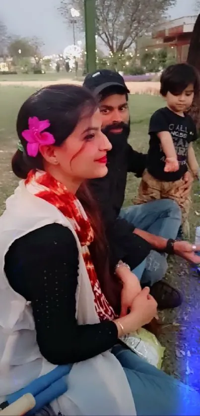 Family relaxing in park with child, flower in hair.