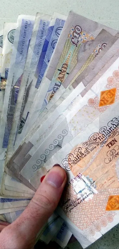 Hand holding fanned British banknotes on light grey background.