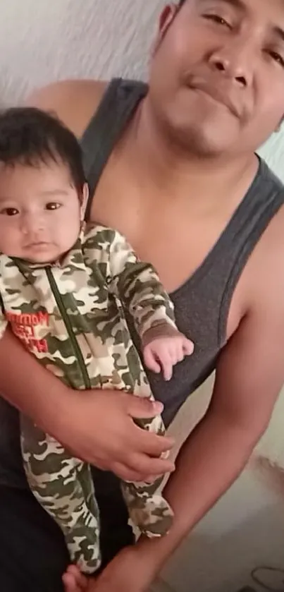 Father holding baby in camouflage outfit, heartfelt moment.