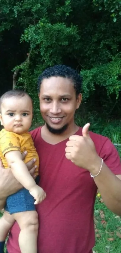 Father holding baby in lush green setting.