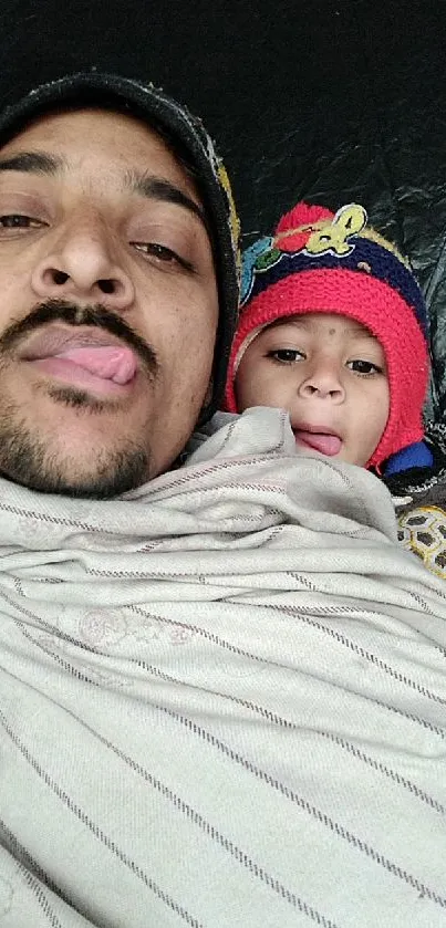 Father and child bundled in warm clothing, sticking tongues out playfully.