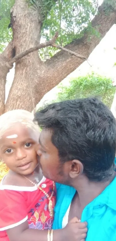 Father and child embracing under a large tree with lush greenery.