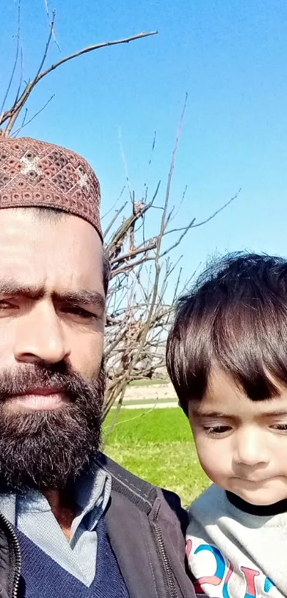 Father holding son in a sunny field with a blue sky.