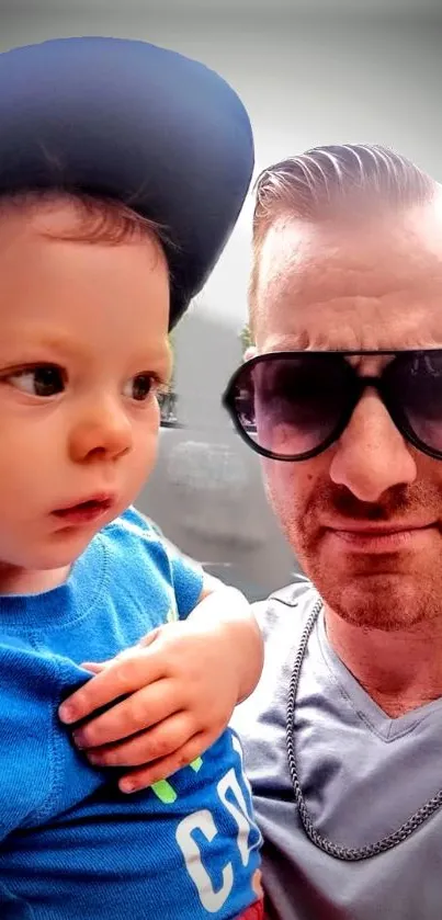 Father and son smiling in a casual photo with sunglasses and cap.