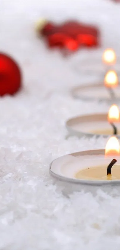 Festive Christmas candles and red ornaments on snowy ground.