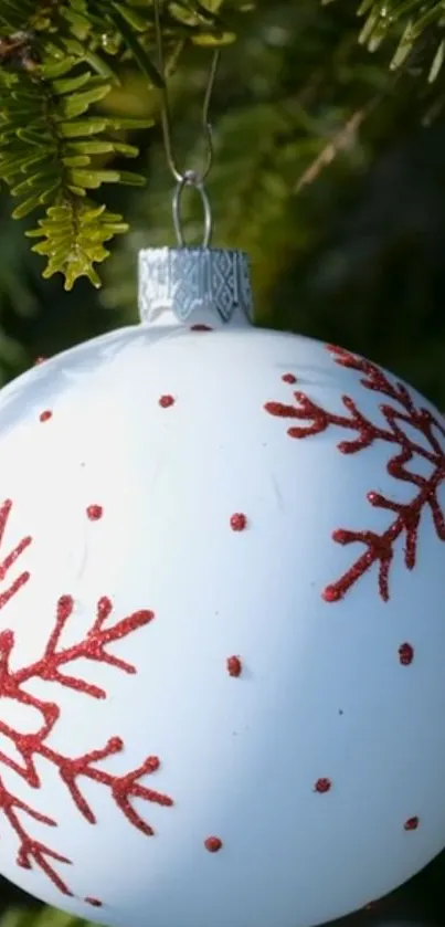 White Christmas ornament with red snowflake patterns on pine branches.