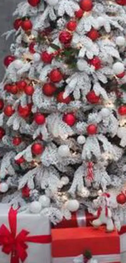 Snow-covered Christmas tree with red ornaments and gifts at the base.