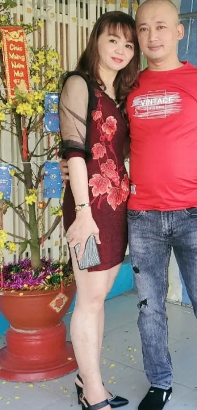 Couple in festive red attire beside a New Year tree.