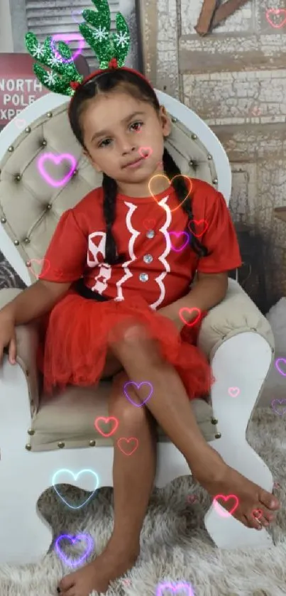 Child in red with antlers on white chair, festive backdrop.