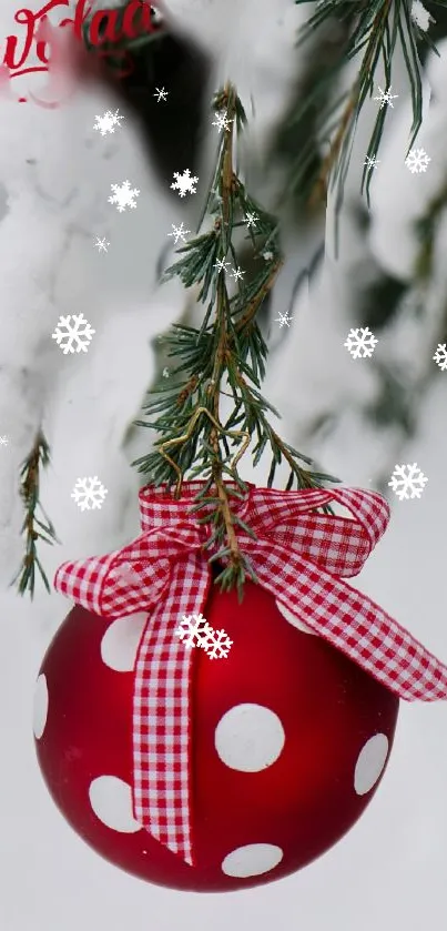 Red polka dot ornament with checkered ribbon hanging on a snowy tree branch.