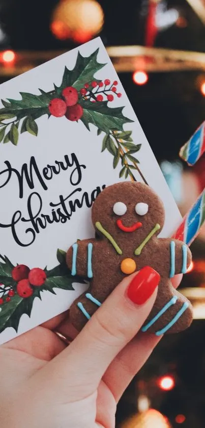 Hand holding a gingerbread man and candy cane with 'Merry Christmas' card.