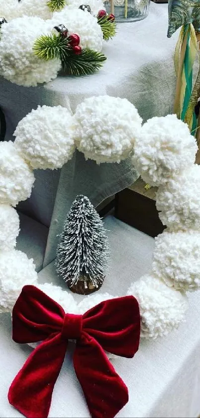 Festive holiday wreath with red bow and pom-poms displayed on a table.