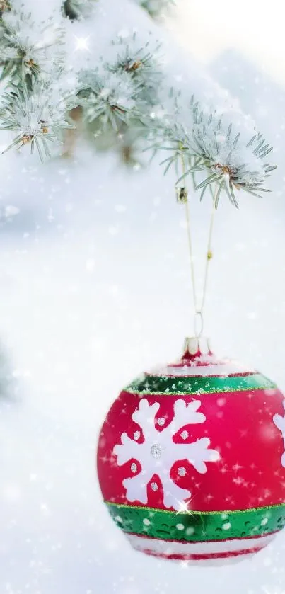 Red snowflake Christmas ornament hanging on snow-covered branch.