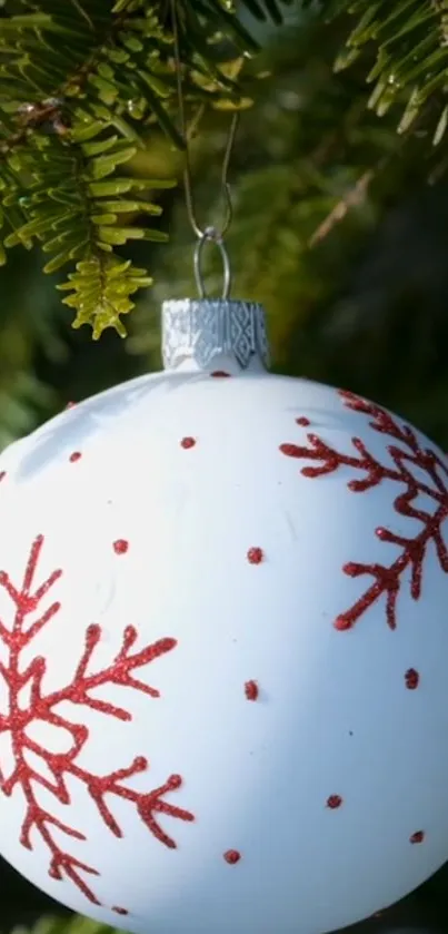 White ornament with red snowflakes on green pine branches.