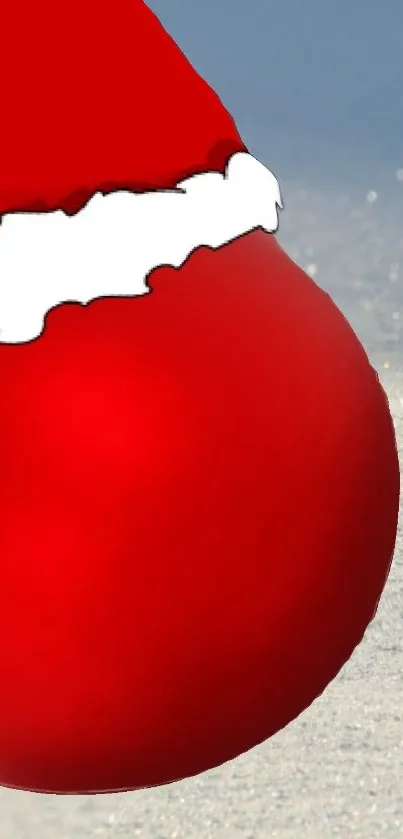 Red Christmas ornament with Santa hat on sandy background.