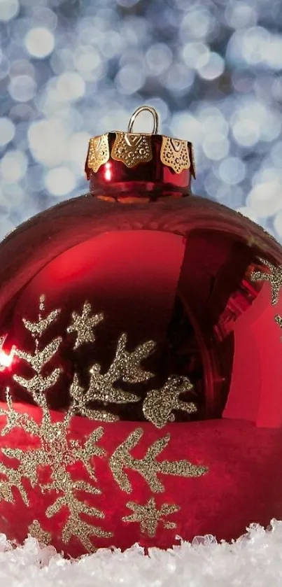 Red Christmas ornament with gold snowflake on snowy surface.