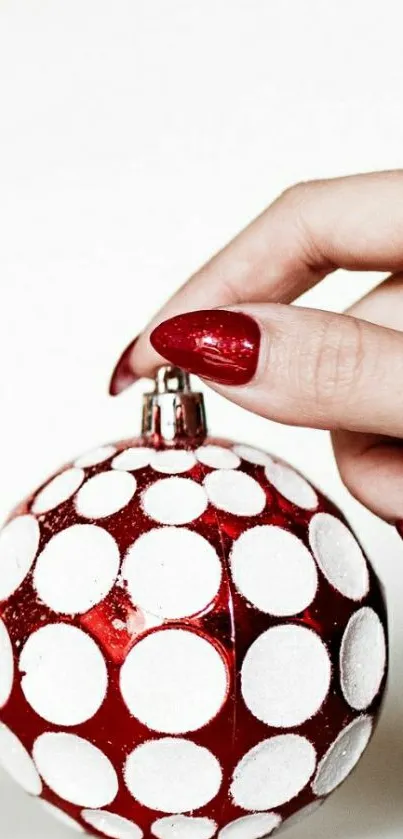 Hand holding red and white polka dot ornament, festive wallpaper design.