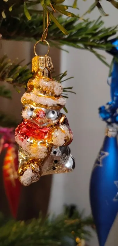 Festive snowman ornament hanging on a decorated Christmas tree branch.