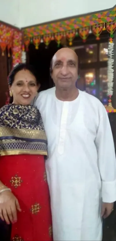 Smiling couple in traditional attire with festive backdrop.