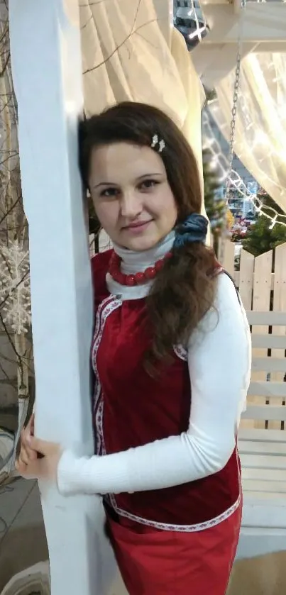 Woman in festive red dress standing near white column indoors.