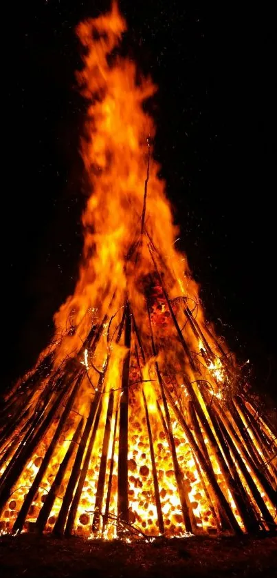 A vibrant, tall bonfire fiercely burns against a dark night sky.