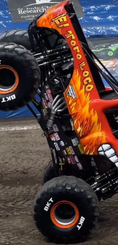 Monster truck performing stunt on dirt track with fiery design.