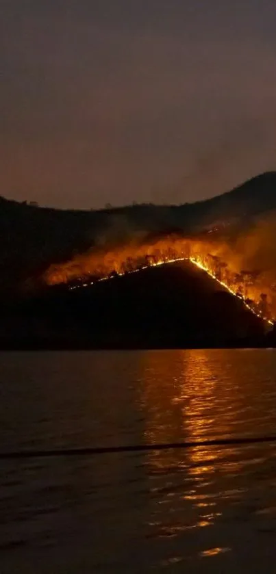 Mountain landscape with orange fire reflection on water at night.