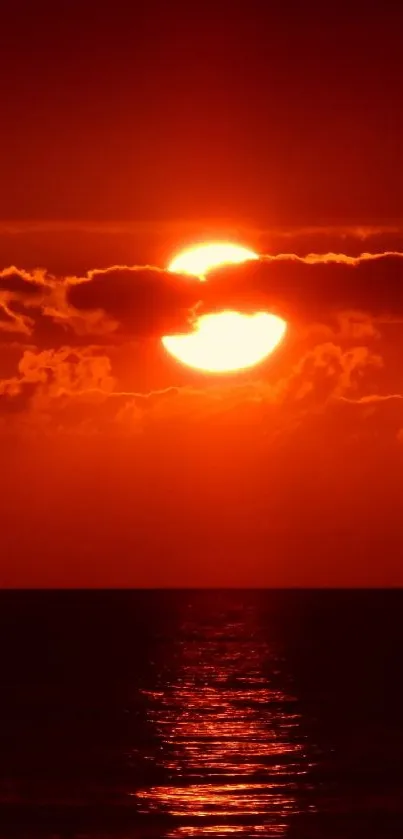 Fiery red sunset over ocean with glowing sky and water reflection.