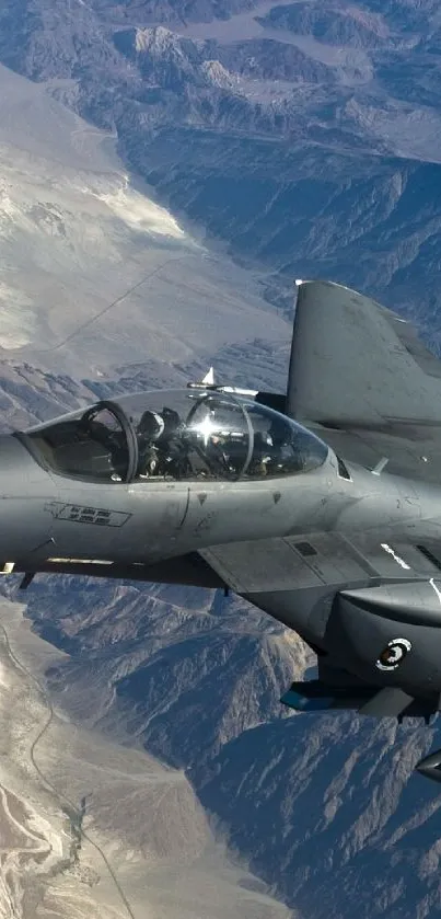 A fighter jet flying above rugged, mountainous terrain.