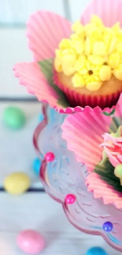 Floral cupcakes with pink wrappers and vibrant icing flowers on a glass stand.