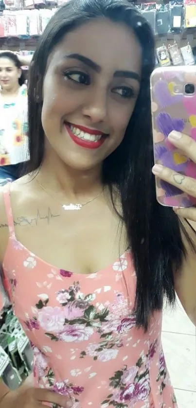 Woman in floral dress, smiling in store, taking a mirror selfie.
