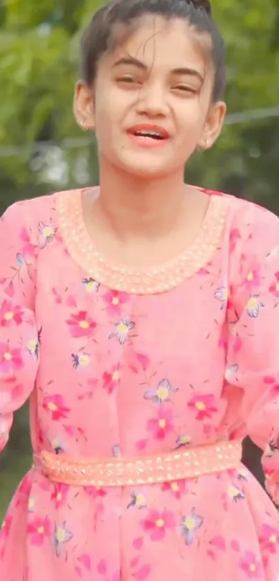 Girl in a floral pink dress with green foliage background.