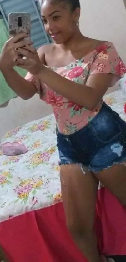 Woman taking a selfie in a floral top and denim shorts.