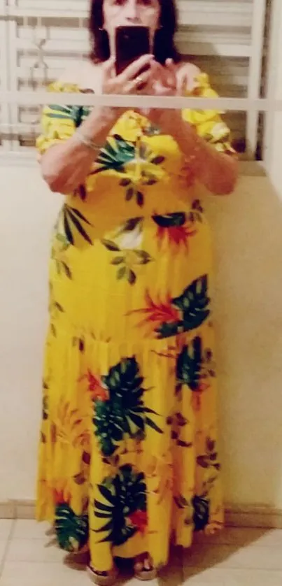 Woman in vibrant yellow floral dress taking selfie in mirror.