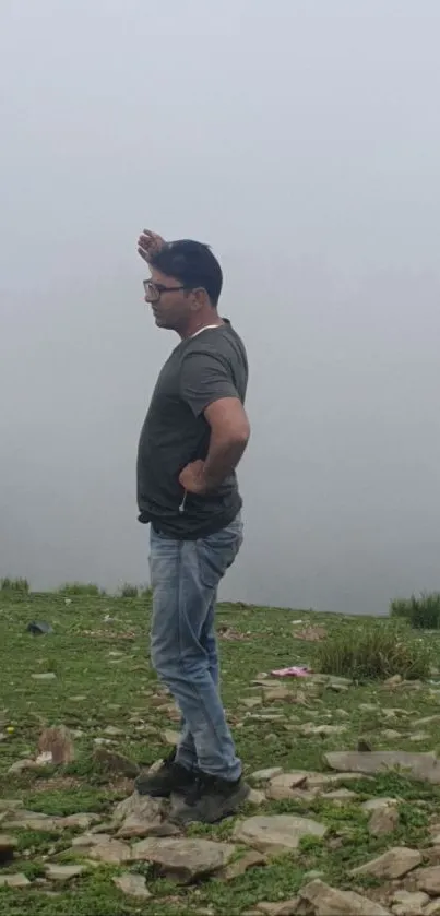 Man standing on a foggy hilltop with mist enveloping the background.