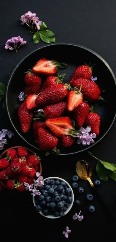 A vibrant arrangement of strawberries, raspberries, and blueberries on a black background.