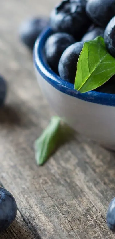 A bowl of fresh blueberries with green leaves on a rustic table.