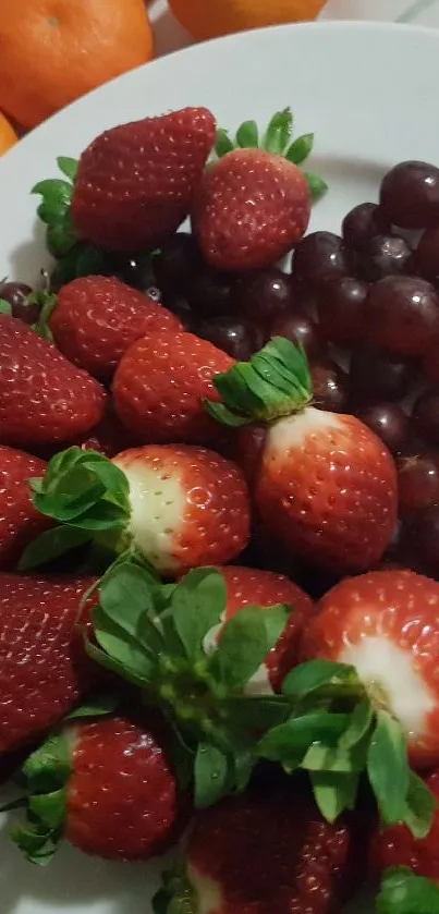 A vibrant mobile wallpaper featuring a fresh fruit platter with strawberries and grapes.