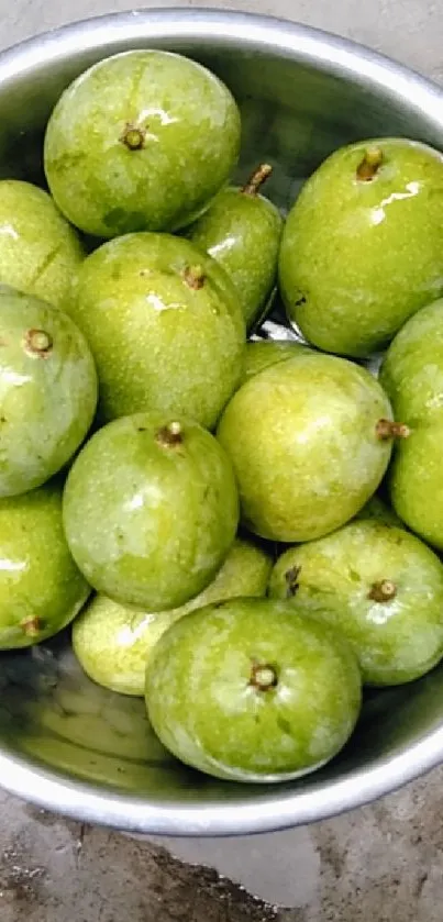 A bowl filled with fresh green mangoes on a concrete surface.