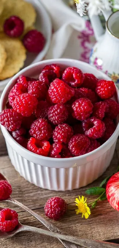 Bowl of fresh raspberries with daisies and apples on wooden background.